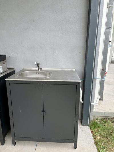 Évier extérieur en inox sur meuble gris raccordé à l'eau et à l'évacuation